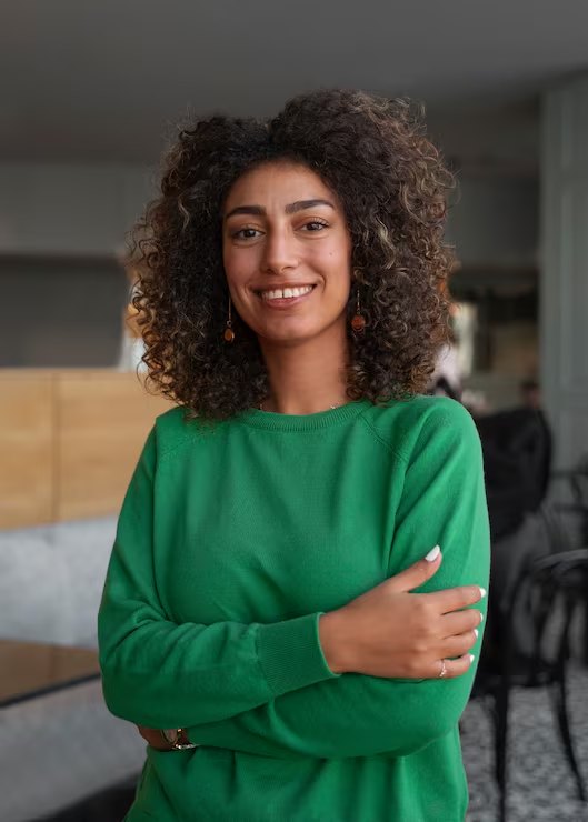 Retrato de uma mulher sorridente de braços cruzados, em ambiente claro e acolhedor